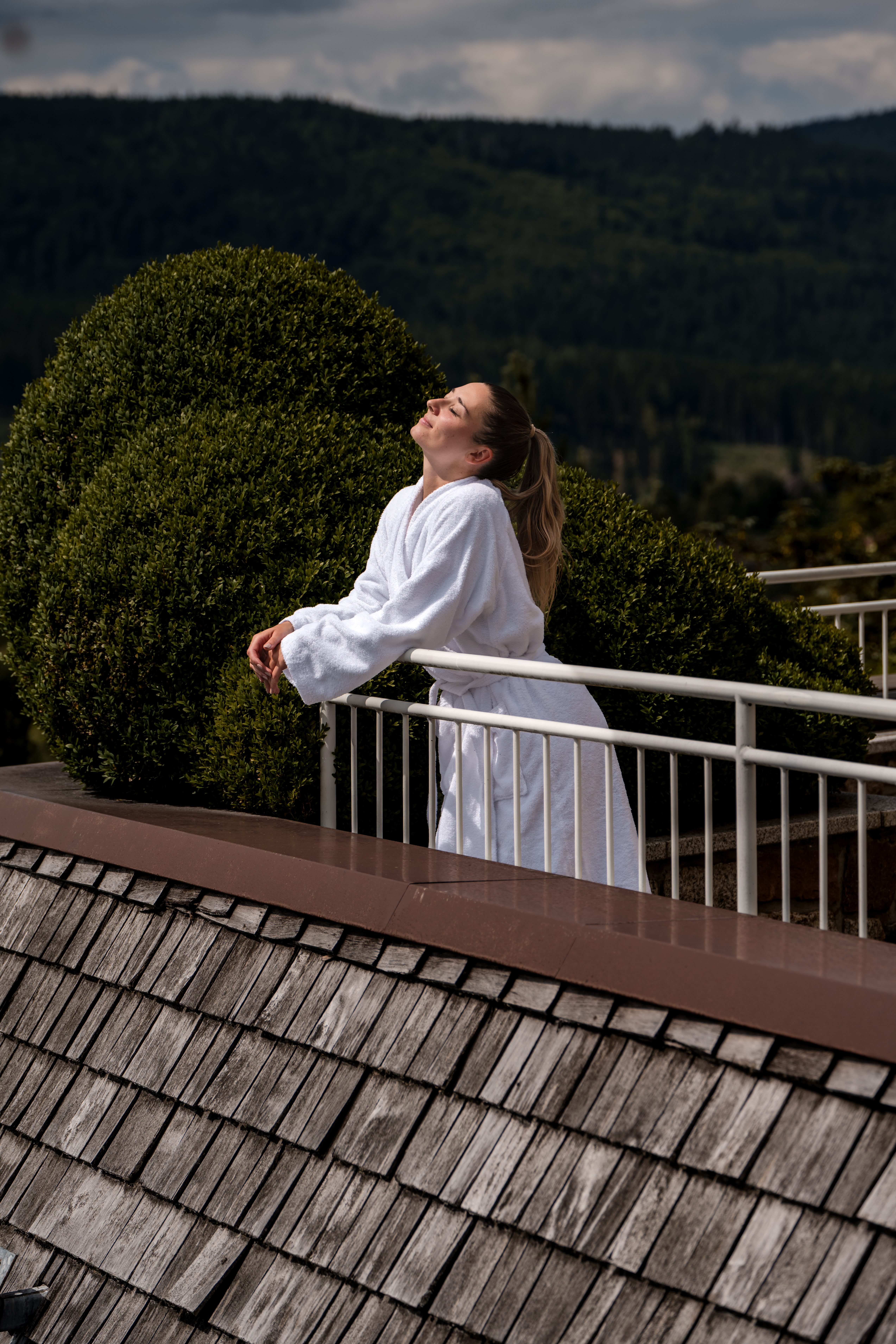 Frau auf Terasse die am Geländer lehnt und das Gesicht in die Sonne streckt