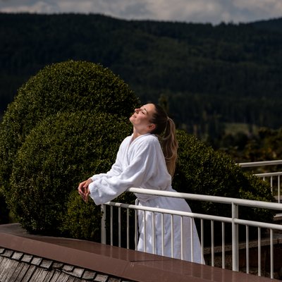 Frau auf Terasse die am Geländer lehnt und das Gesicht in die Sonne streckt