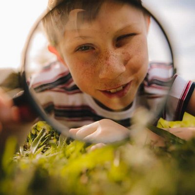 Ein neugieriger Junge untersucht mit einer Lupe kleine Insekten oder Pflanzen in der Natur.