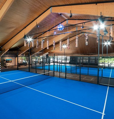 Zwei nebeneinanderliegende Padel-Courts unter einer beeindruckenden Holzarchitektur.