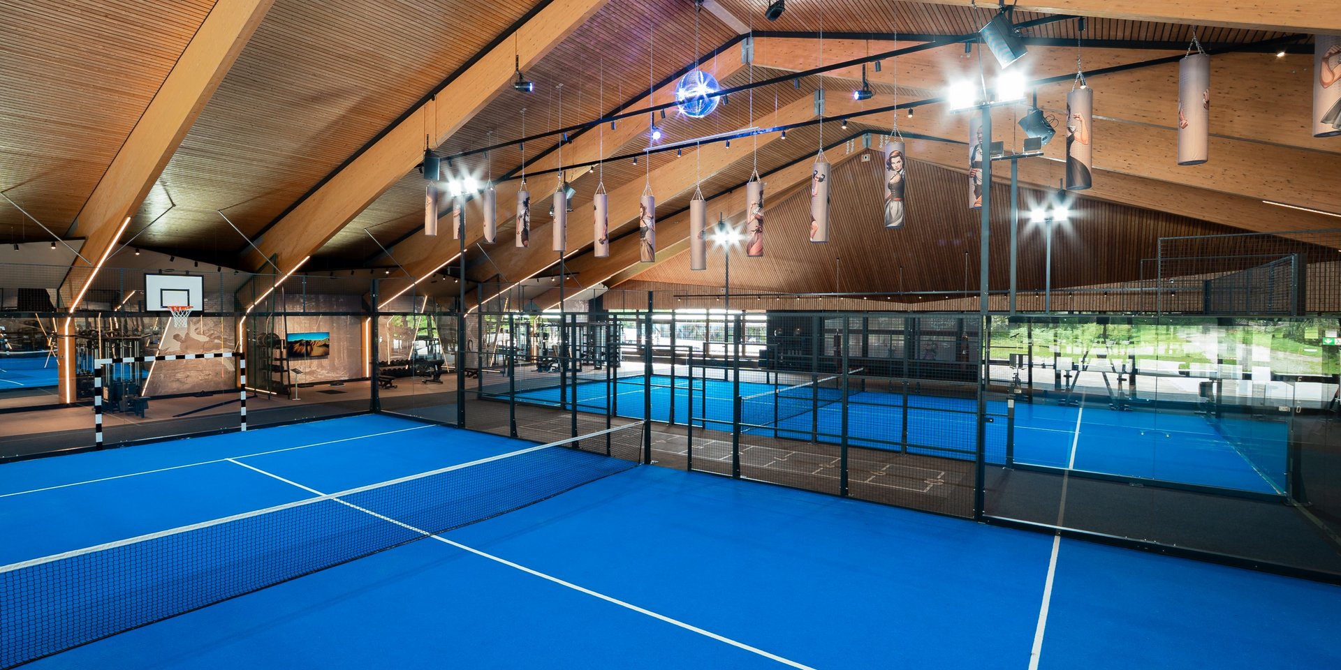 Zwei nebeneinanderliegende Padel-Courts unter einer beeindruckenden Holzarchitektur.