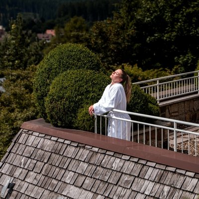 Eine Frau im weißen Bademantel genießt die Aussicht von der Terrasse des Wellnesspools im Hotel Vier Jahreszeiten.