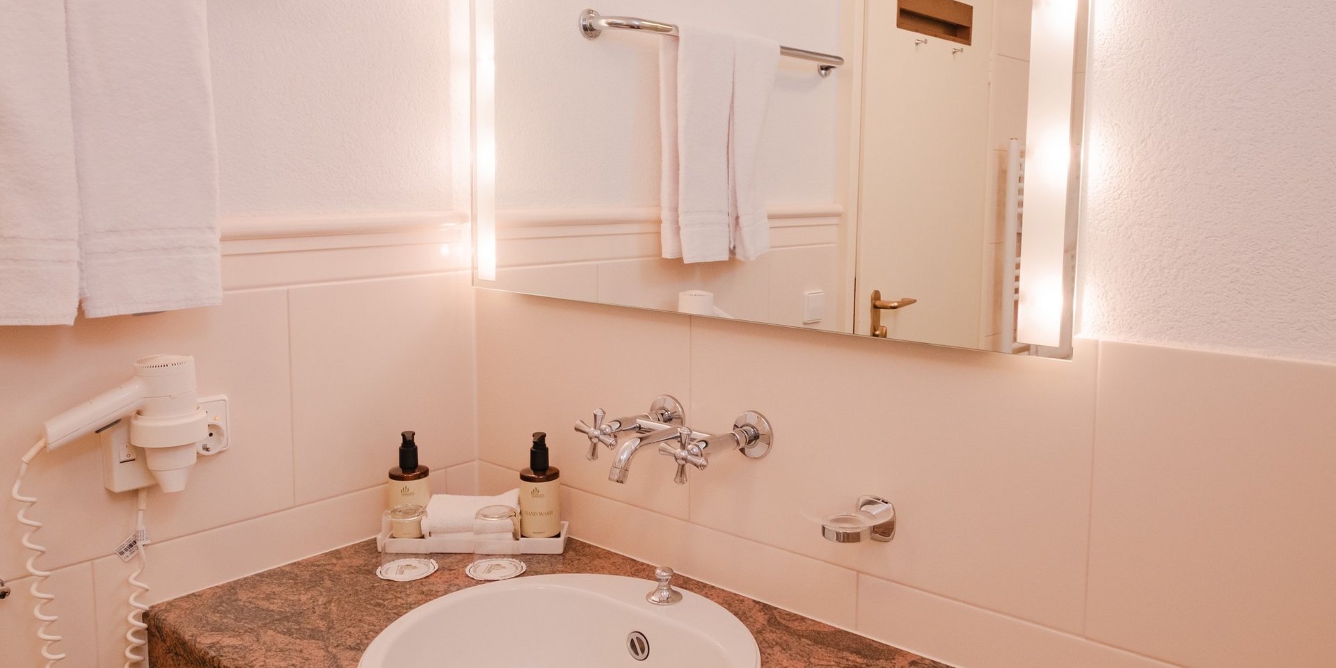 Modernes Badezimmer mit beleuchtetem Spiegel und Waschtisch in Naturstein-Optik.