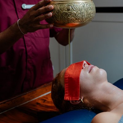 Therapeut gießt behutsam warmes Öl bei einer Ayurveda-Behandlung im Hotel Vier Jahreszeiten am Schluchsee aus einer Schale.