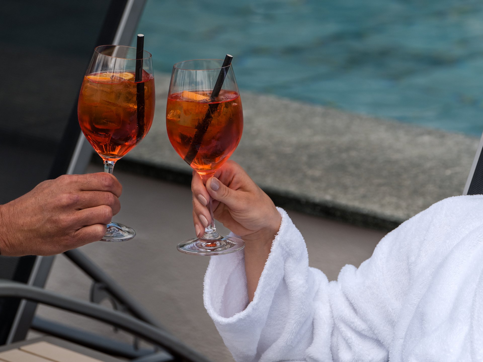 Two people toasting with a drink by the pool