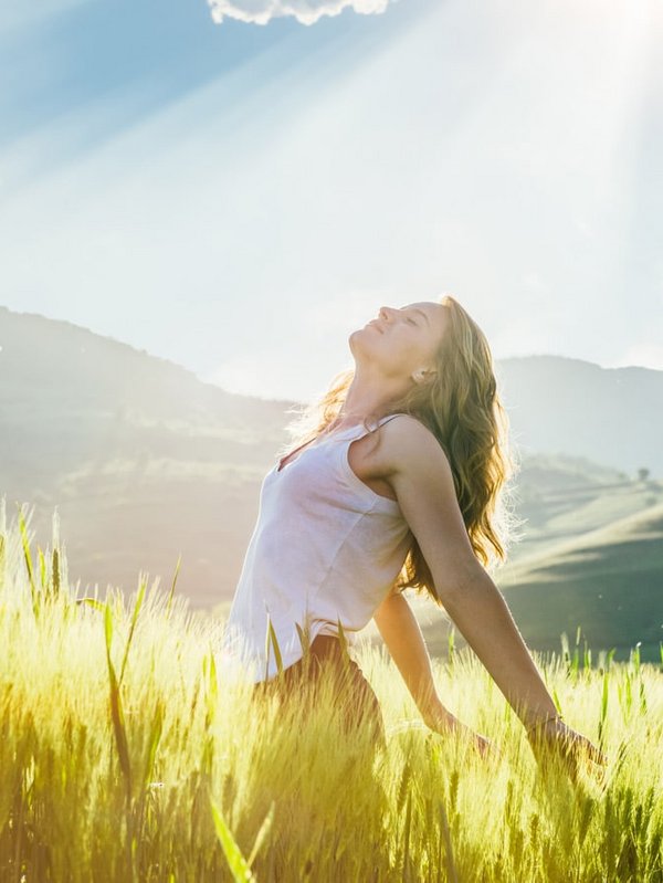 Eine Frau steht mit ausgebreiteten Armen auf einer blühenden Sommerwiese.
