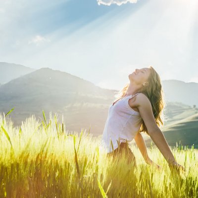 Eine Frau steht mit ausgebreiteten Armen auf einer blühenden Sommerwiese.