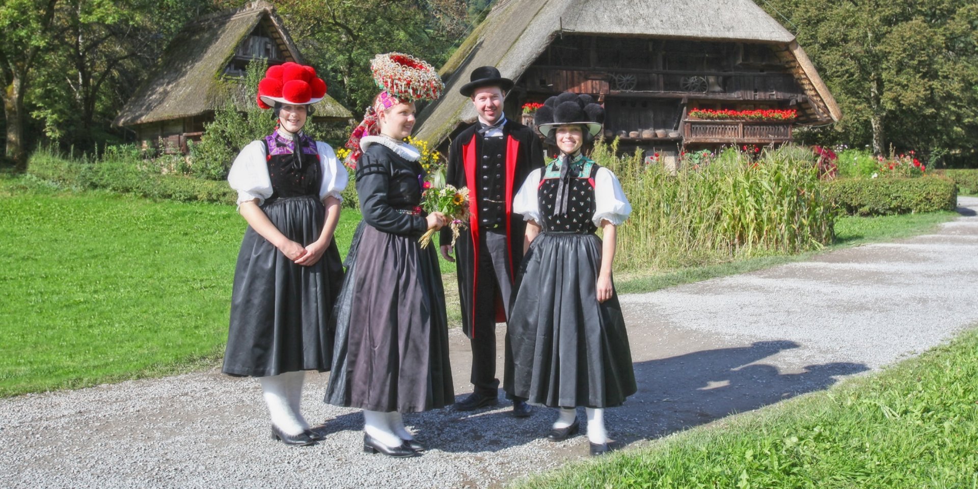 Eine Gruppe in traditioneller Schwarzwälder Tracht vor einem historischen Bauernhaus.