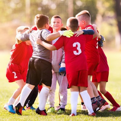 Eine Gruppe von Kindern in roten Trikots jubelt gemeinsam nach einem Fußballspiel auf dem Rasenplatz.