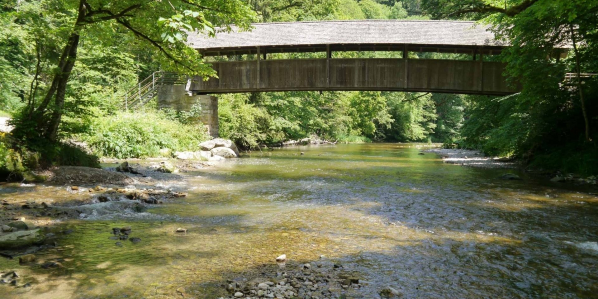 Eine überdachte Holzbrücke über einen Fluss als Teil eines Schwarzwälder Wanderwegs.