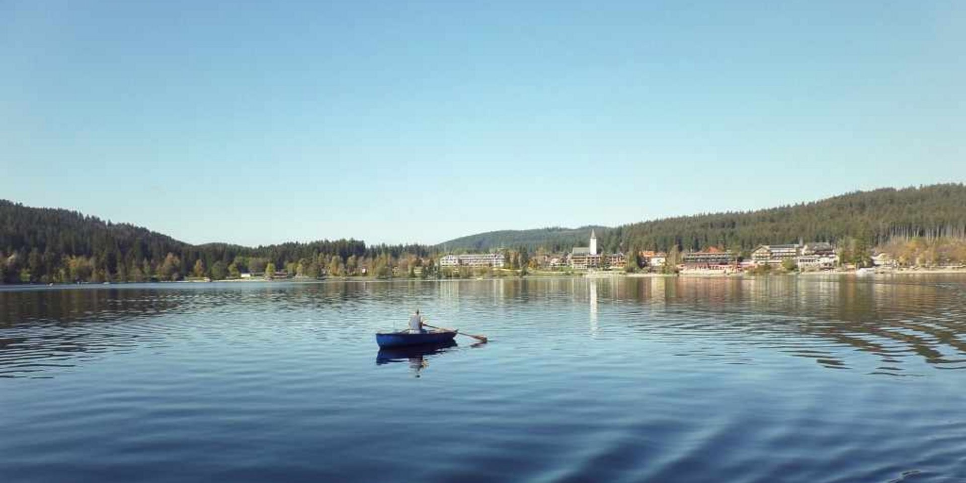 Ein Mann rudert in einem kleinen Boot auf einem ruhigen See im Schwarzwald.