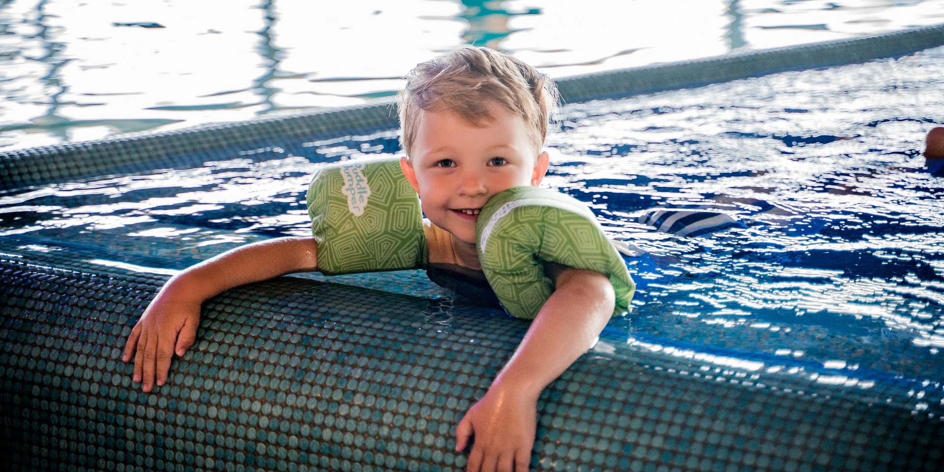 Kind mit Schwimmfluegeln am Beckenrand