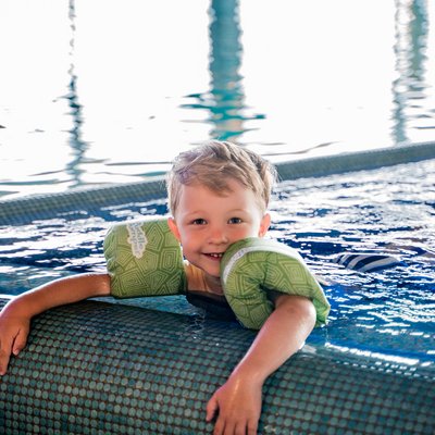Kind mit Schwimmfluegeln am Beckenrand