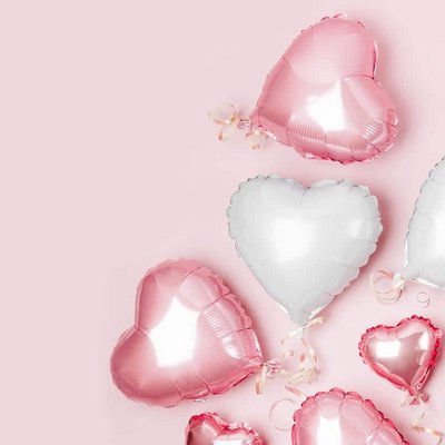 Mehrere rosa und silberne Herzluftballons schweben vor einem zartrosa Hintergrund.