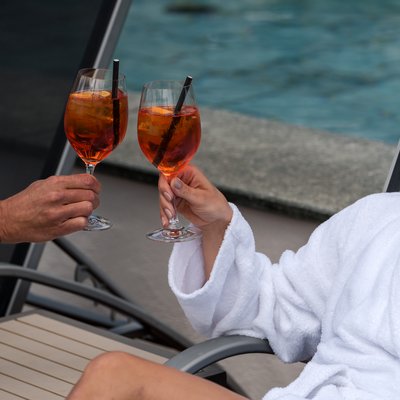 Person in Bademantel mit aufgestelltem Bein und Cocktail in der Hand