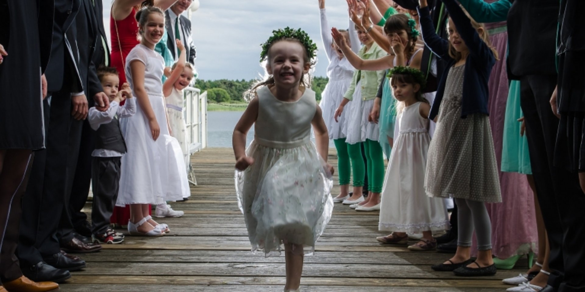 Ein kleines Blumenmädchen läuft fröhlich durch ein Spalier aus klatschenden Hochzeitsgästen.