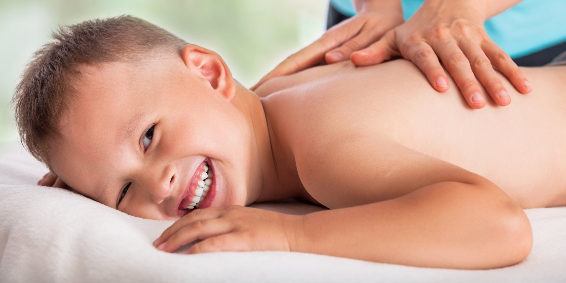 Ein lächelnder Junge genießt eine beruhigende Rückenmassage in einem Wellnessbereich.