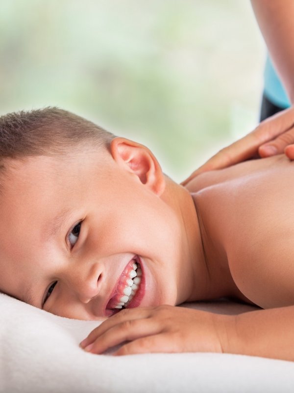 Ein lächelnder Junge genießt eine beruhigende Rückenmassage in einem Wellnessbereich.