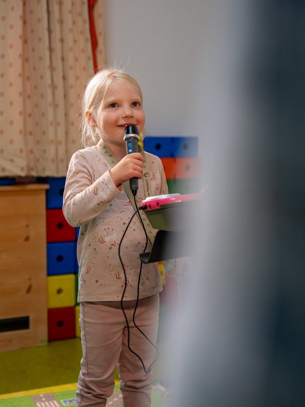 Ein Mädchen singt fröhlich mit einem Mikrofon während des Kinderprogramms im Hotel Vier Jahreszeiten im Schwarzwald.