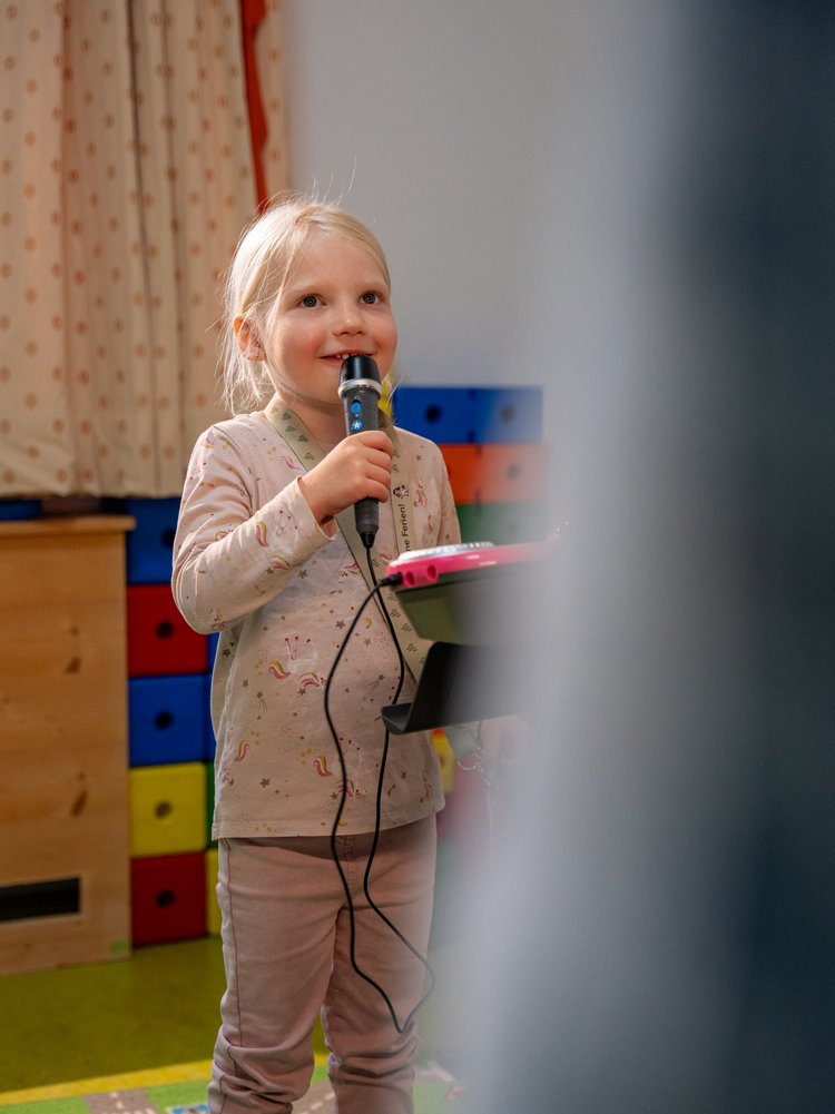 Ein Mädchen singt fröhlich mit einem Mikrofon während des Kinderprogramms im Hotel Vier Jahreszeiten im Schwarzwald.