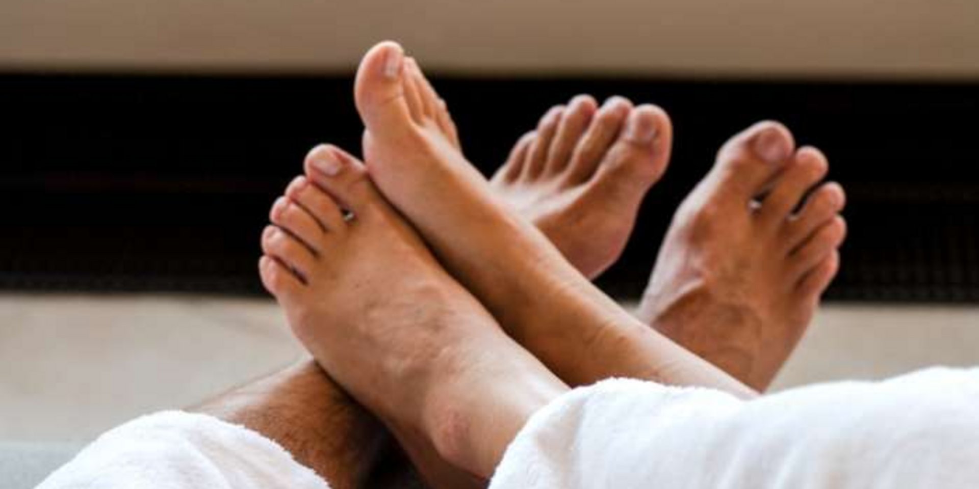 Nahaufnahme der Füße eines Paares, das entspannt unter weißen Handtüchern im Hotel liegt.