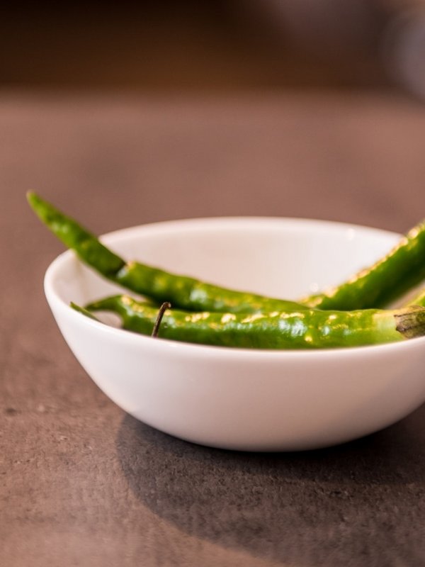 Eine kleine weiße Schale mit frischen grünen Chilischoten auf einer Schieferplatte.