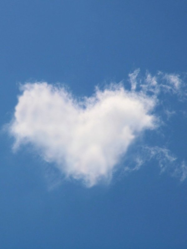 Eine kleine weiße Wolke in Form eines Herzens schwebt am strahlend blauen Himmel