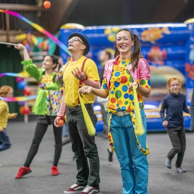 Fröhliche Clowns unterhalten eine Gruppe Kinder mit bunten Ballons in der Indoor-Spielwelt des Hotels Vier Jahreszeiten im Schwarzwald.