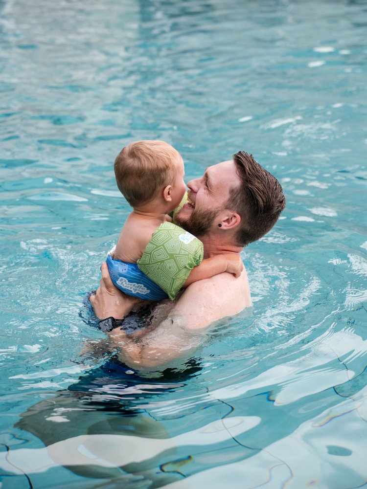 Ein Vater trägt sein Kind im warmen Wasser des hoteleigenen Schwimmbads im Hotel Vier Jahreszeiten.