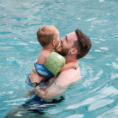 Ein Vater trägt sein Kind im warmen Wasser des hoteleigenen Schwimmbads im Hotel Vier Jahreszeiten.