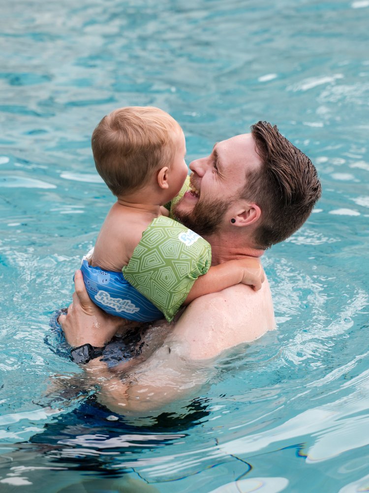 Ein Vater trägt sein Kind im warmen Wasser des hoteleigenen Schwimmbads im Hotel Vier Jahreszeiten.