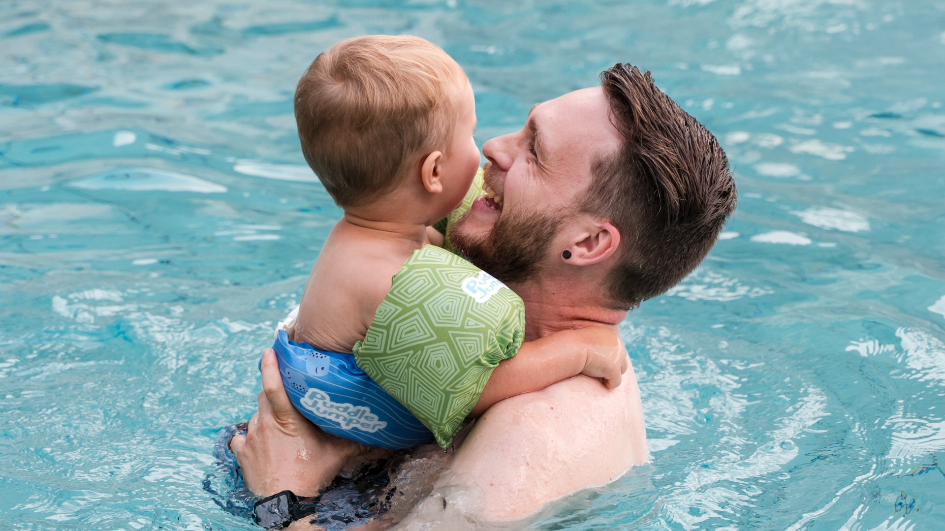 Ein Vater trägt sein Kind im warmen Wasser des hoteleigenen Schwimmbads im Hotel Vier Jahreszeiten.