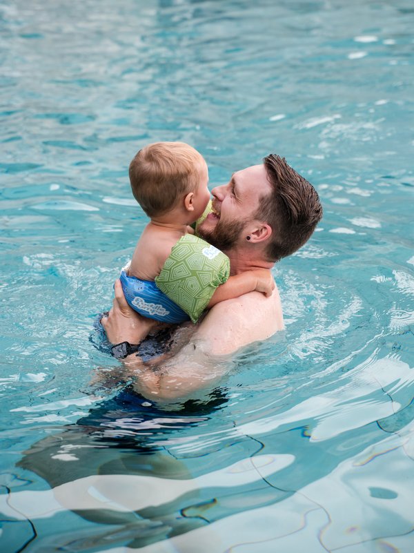 Ein Vater trägt sein Kind im warmen Wasser des hoteleigenen Schwimmbads im Hotel Vier Jahreszeiten.