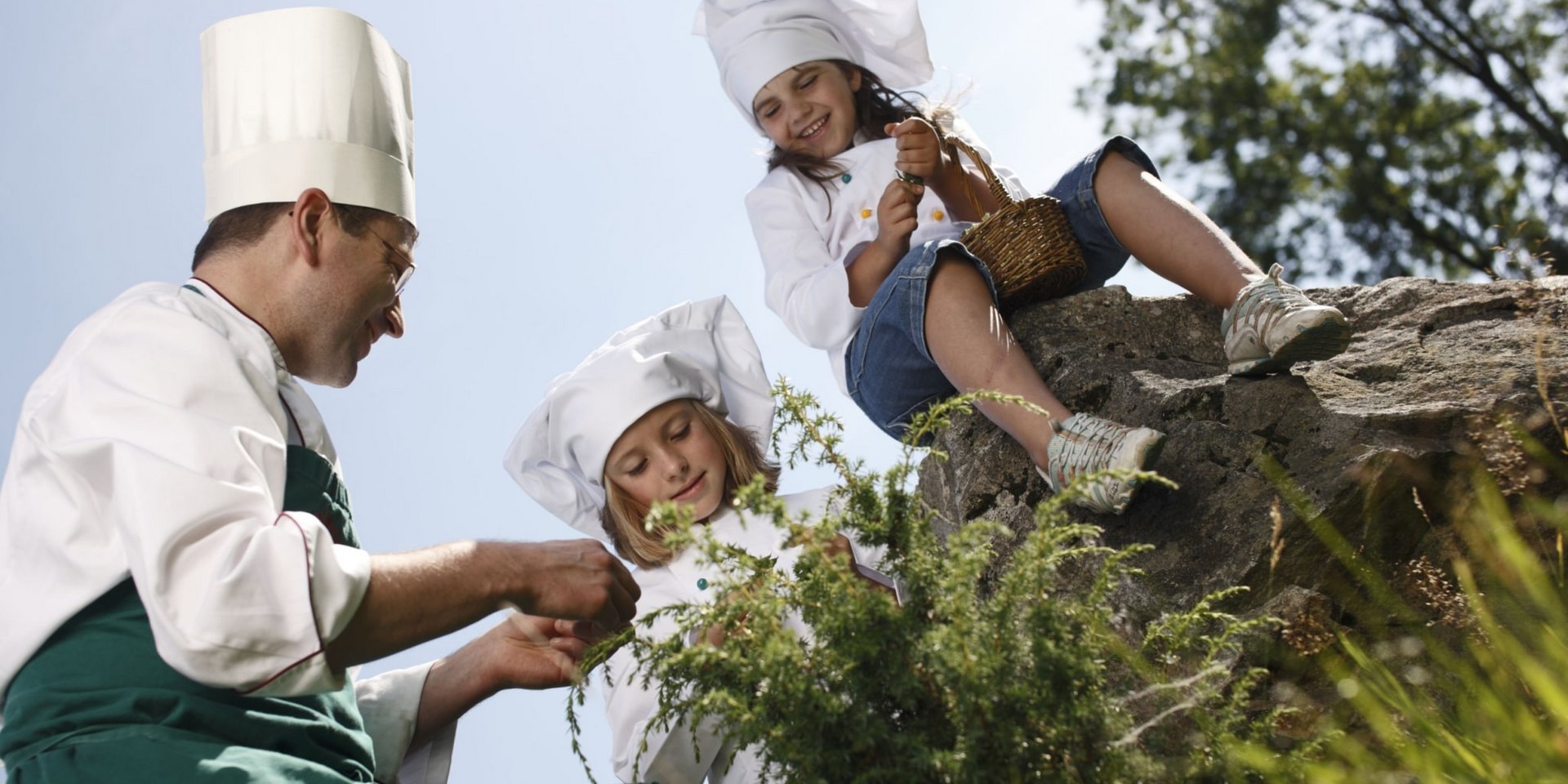 Kinder in Kochmützen lernen gemeinsam mit einem Profi-Koch das Zubereiten gesunder Speisen im Hotel Vier Jahreszeiten.
