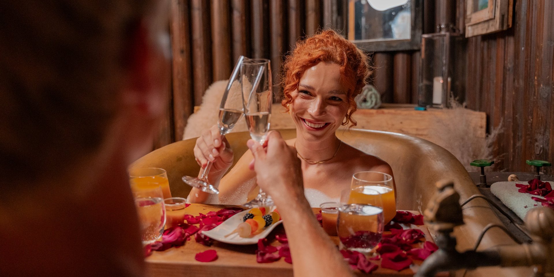 Zwei Gäste stoßen mit Sektgläsern in einer schäumenden Kupferwanne im Wellnessbereich des Hotels Vier Jahreszeiten an.