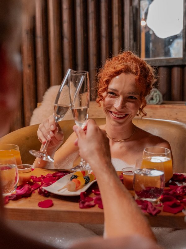 Zwei Gäste stoßen mit Sektgläsern in einer schäumenden Kupferwanne im Wellnessbereich des Hotels Vier Jahreszeiten an.