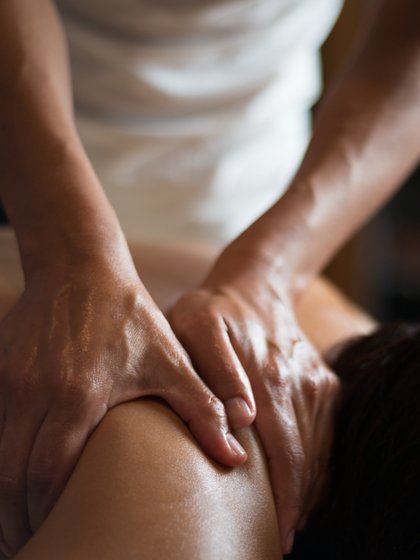 Person liegt auf einer Massageliege und wird von zwei Händen an der Schulter massiert