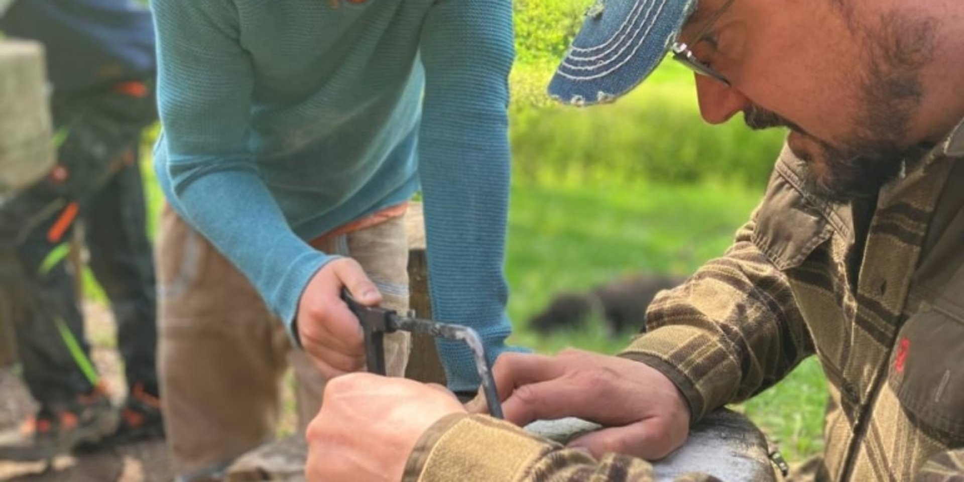 Ein Kursleiter zeigt Kindern in der Natur, wie man sicher mit Werkzeugen und Holz umgeht.