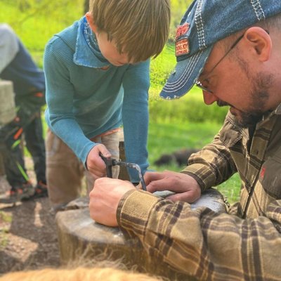 Ein Kursleiter zeigt Kindern in der Natur, wie man sicher mit Werkzeugen und Holz umgeht.