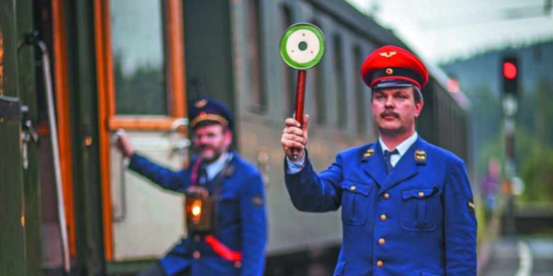 Eine Zugbegleiterin in blauer Uniform winkt zur Abfahrt aus einem historischen Waggon im Schwarzwald.