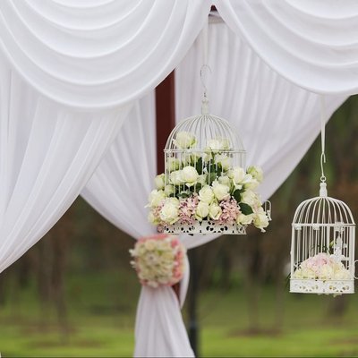 Ein festlich dekorierter Hochzeitsbogen mit weißen Vorhängen und Blumengestecken im Freien.