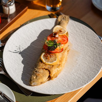 Frisch zubereiteter, ganzer Fisch mit Zitrone und Beilage, serviert auf einem weißen Teller im Restaurant.