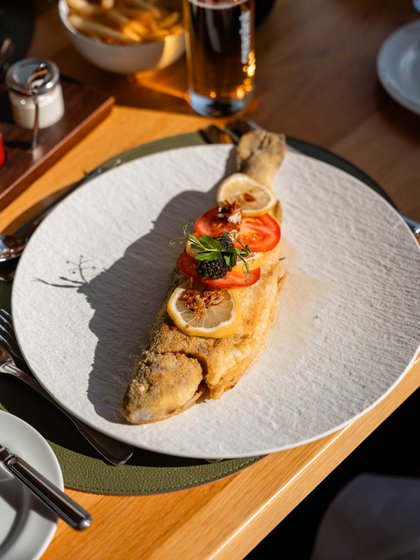 Frisch zubereiteter, ganzer Fisch mit Zitrone und Beilage, serviert auf einem weißen Teller im Restaurant.