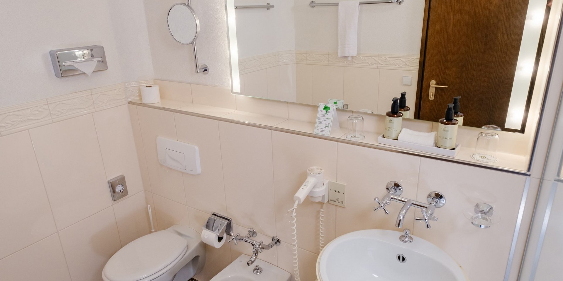 Modernes Badezimmer mit großem, beleuchtetem Spiegel im Hotel Vier Jahreszeiten am Schluchsee.