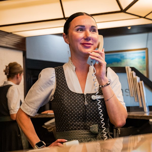 Eine lächelnde Mitarbeiterin am Telefon im Servicebereich des Hotels Vier Jahreszeiten kümmert sich um die Wünsche der Gäste.