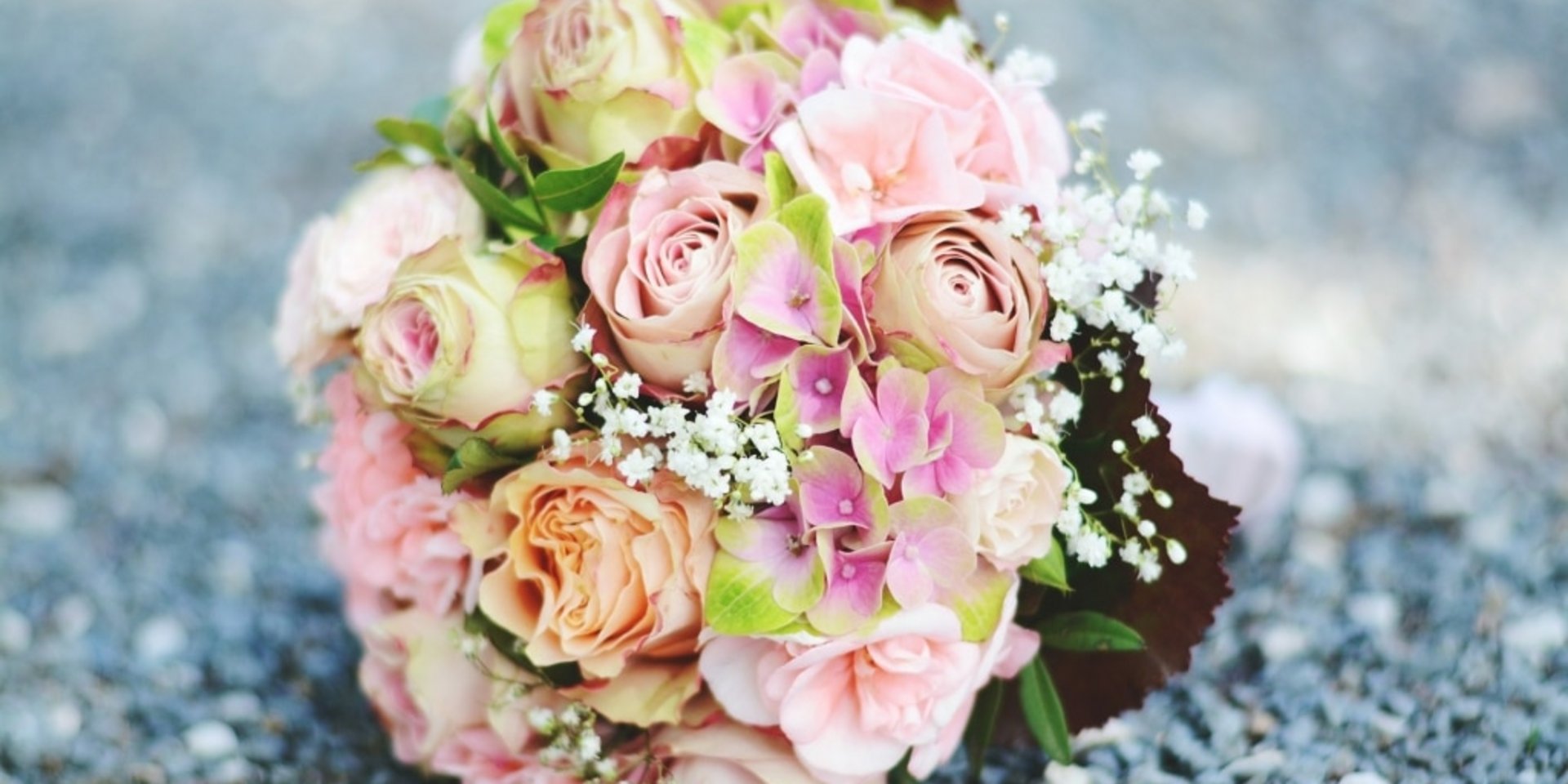Ein eleganter Brautstrauß aus rosa und weißen Rosen liegt auf einem steinigen Untergrund.