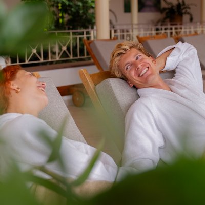 Zwei Gäste entspannen in flauschigen Bademänteln auf bequemen Liegen im Spa des Hotels Vier Jahreszeiten im Schwarzwald.