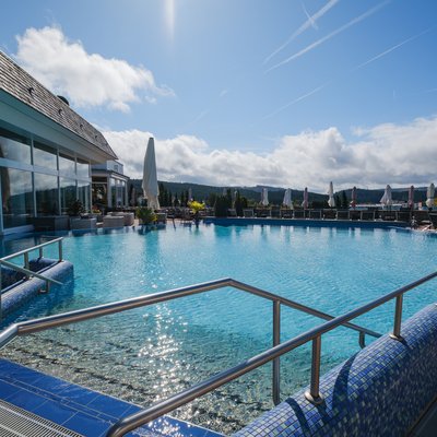 Beheizter Außenpool mit Blick auf die umliegende Natur und Liegeflächen unter blauem Himmel.