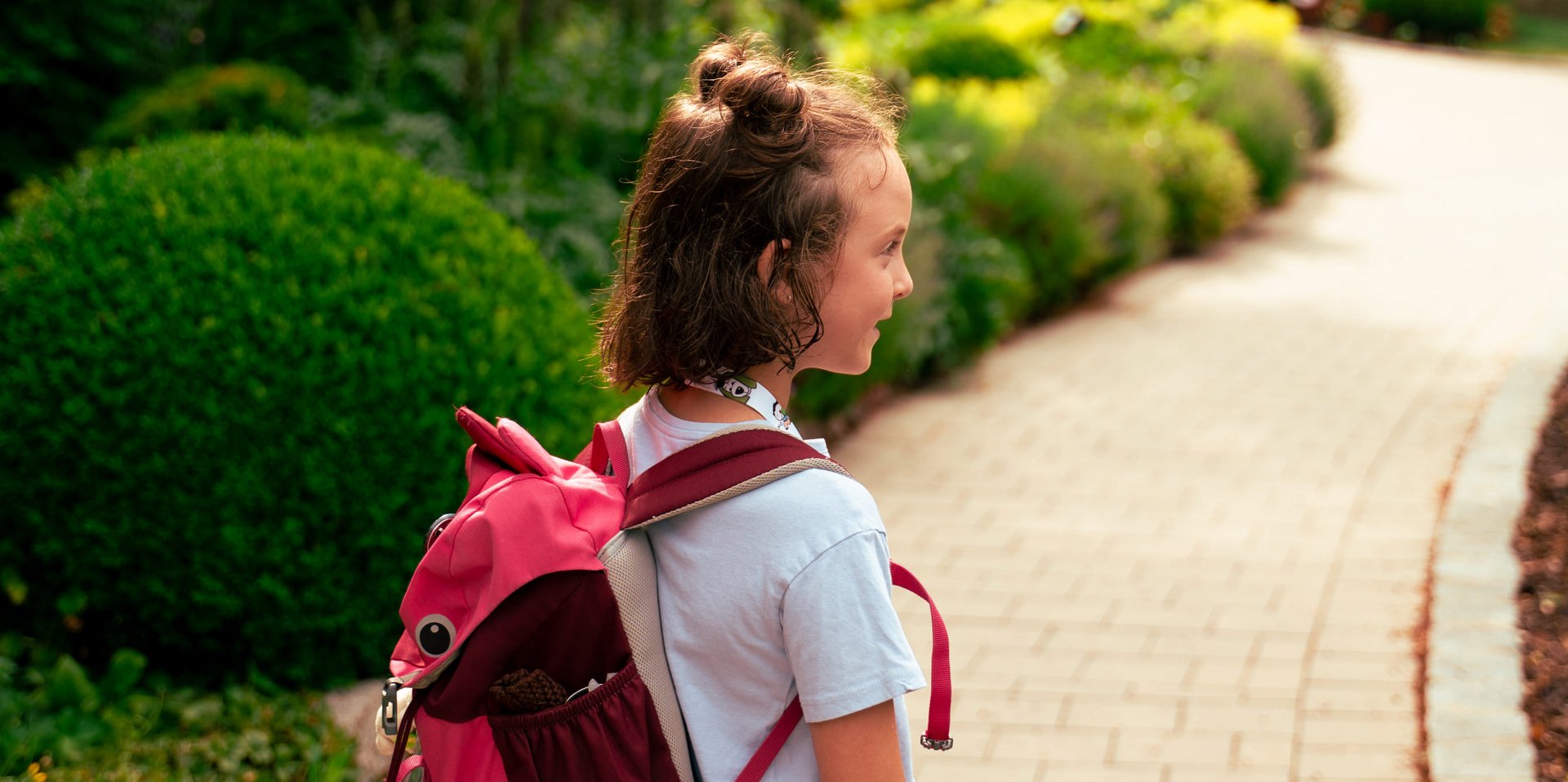 Ein Mädchen mit Rucksack spaziert durch eine gepflegte Parkanlage.