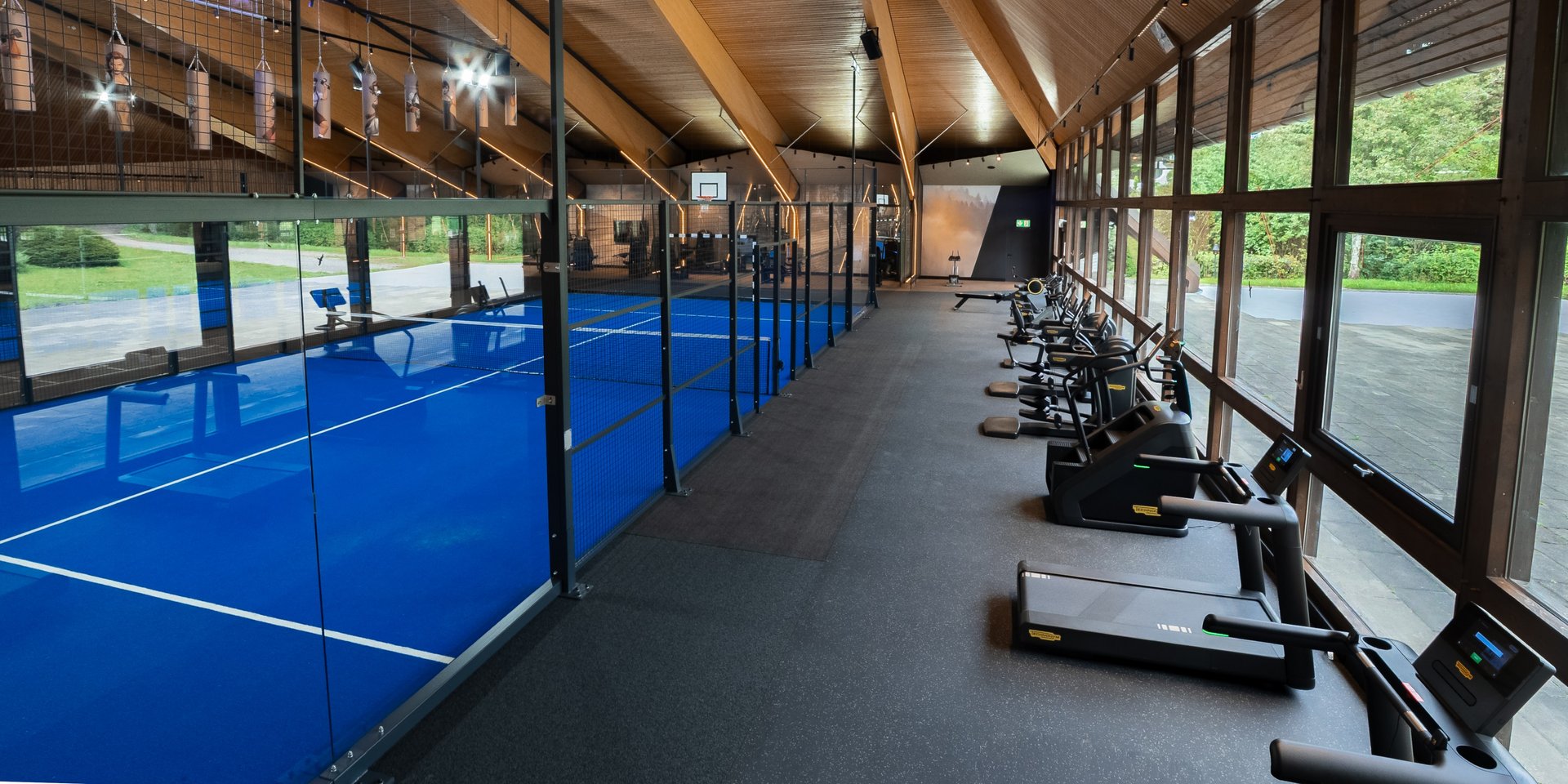 Kombination aus Padel-Platz und Fitnessbereich mit Laufbändern in der Sporthalle.